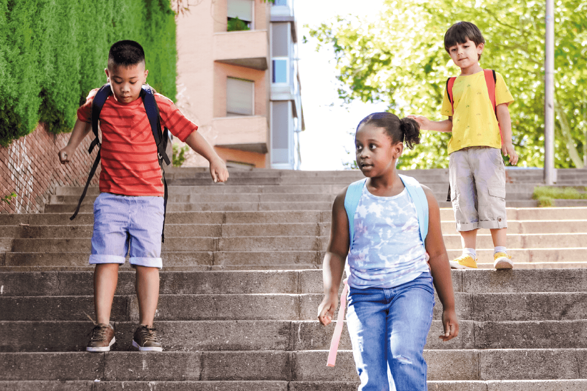 Tres niños estudiantes bajando escalas, en camino de inclusión