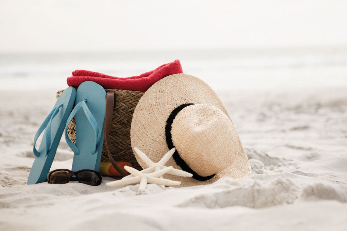 Imagen de una playa, un sombrero, unas sandalias y un bolso de alguien que esta de vacaciones