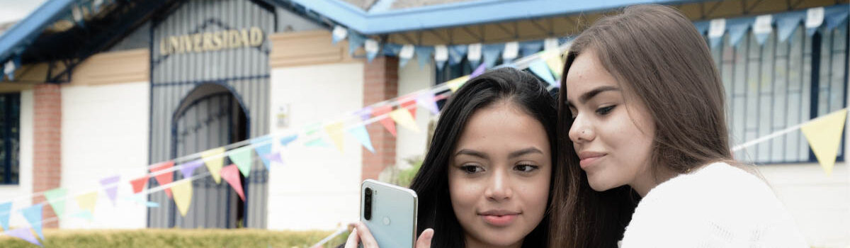 Dos mujeres jóvenes mirando el periódico escolar del Cibercolegio en su celular.