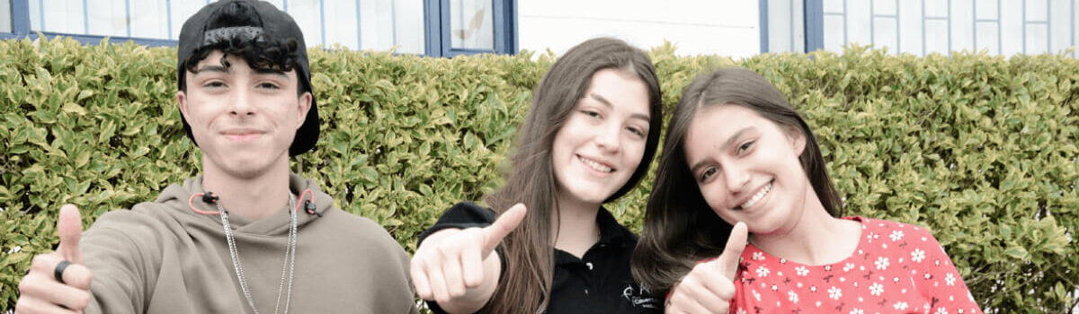 Fotografía de dos jóvenes alumnas y un alumno del Cibercolegio en el Campus de la Fundación Universitaria Católica del Norte, se encuentran sentados en la zona verde y reflejan sentirse felices disfrutando de su colegio. Una de las alumnas es la personera estudiantil electa en el año 2022.